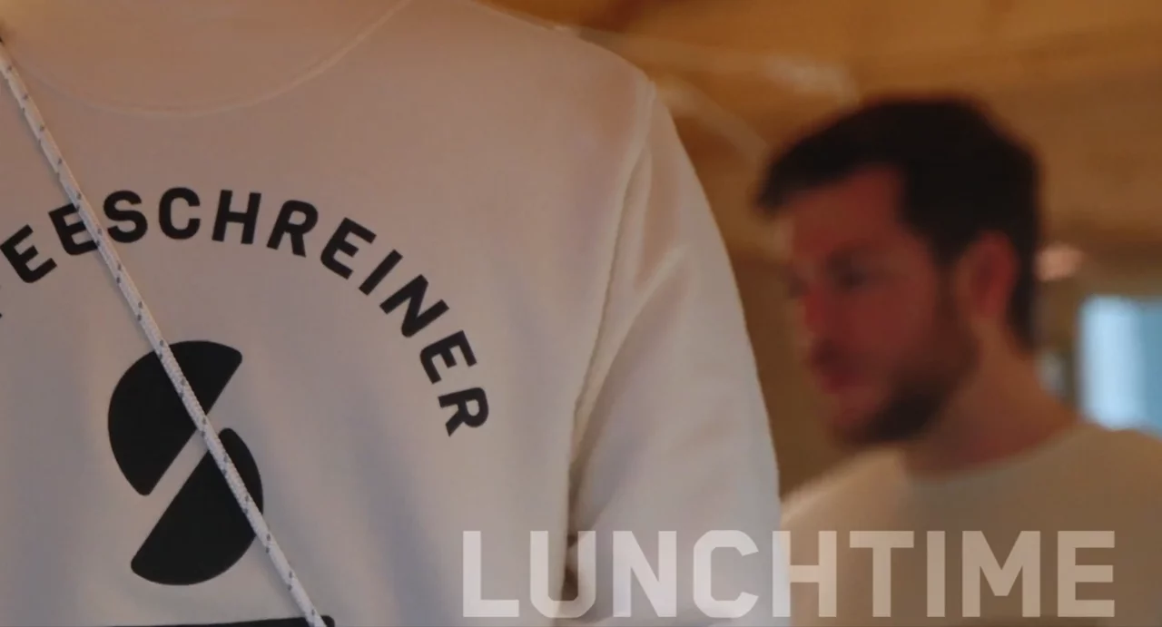 Ein angeschnittener Pulli von hinten deutet an, dass es sich um unseren Kooperationspartner "Kaffee Schreiner" handelt. Unten rechts stehen die Lettern "Lunchtime" angeschnitten.