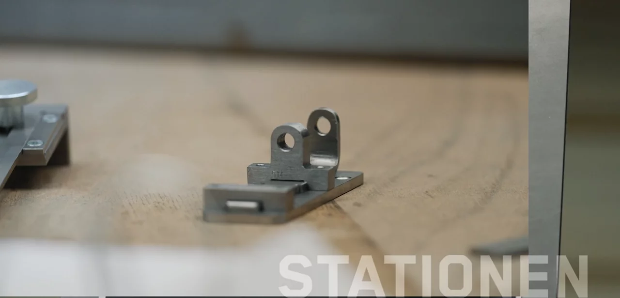 Ein Blechteil liegt auf einem hölzernen Untergrund. Unten rechts steht in großen Lettern "Station" geschrieben.