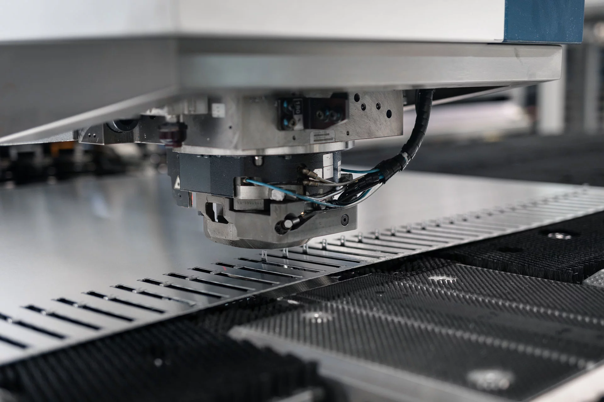 Nahaufnahme auf den Maschinenkopf einer Stanz-Lasermaschine von TRUMPF samt gestanztem Blechteil mit Umformungen.