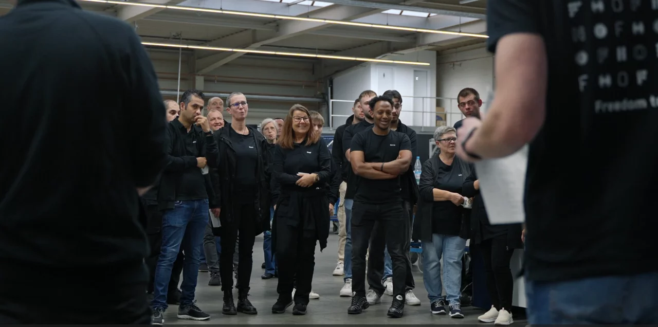 Aus Perspektive der Vortragenden sieht man HOF-Mitarbeiter in der Fertigung im HOF-Shirt zuhörend vor sich stehen.