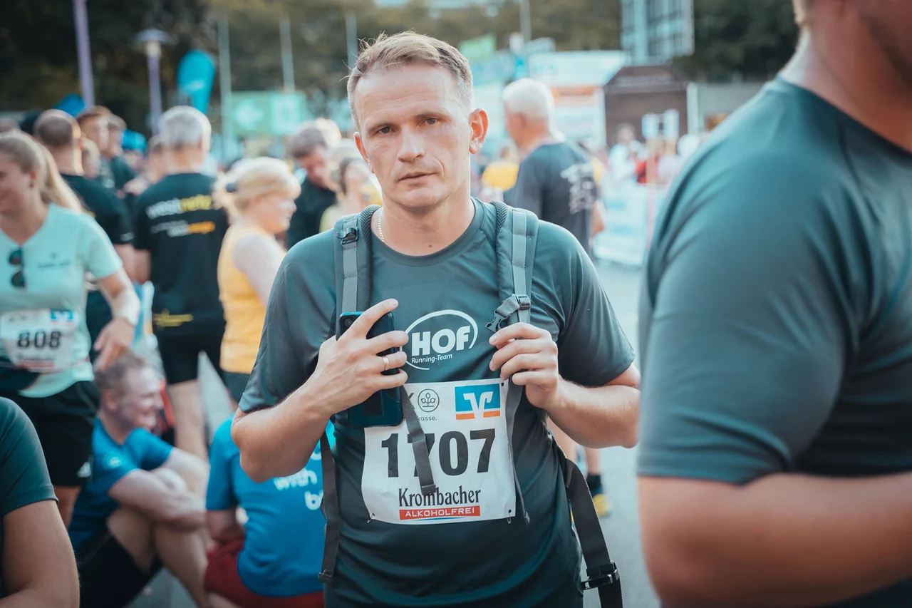 Ein HOF-Mitarbeiter guckt etwas erschöpf in die Kamera. Er trägt sein HOF-Laufshirt mit seiner Startnummer.