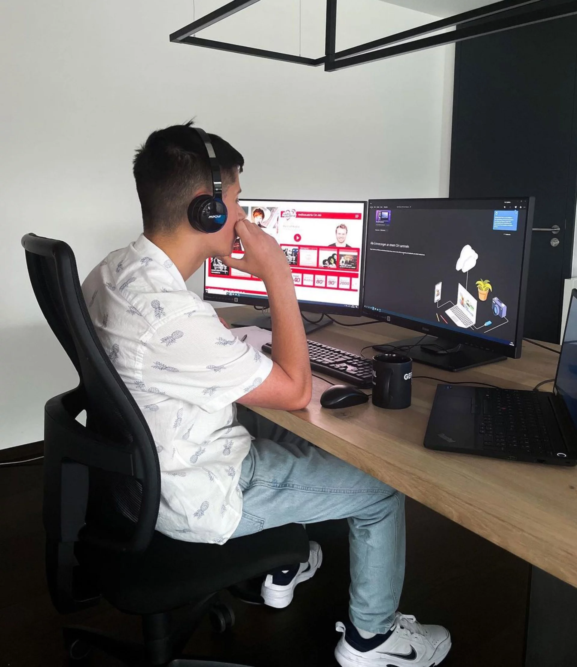 Der Azubi sitzt mit Kopfhörern an seinem Schreibtisch und schaut fokussiert auf seine zwei Monitore. Auf dem Bildschirm ist die Seite des österreichischen Radiosenders geöffnet, bei dem er sein Auslandssemester gemacht hat.