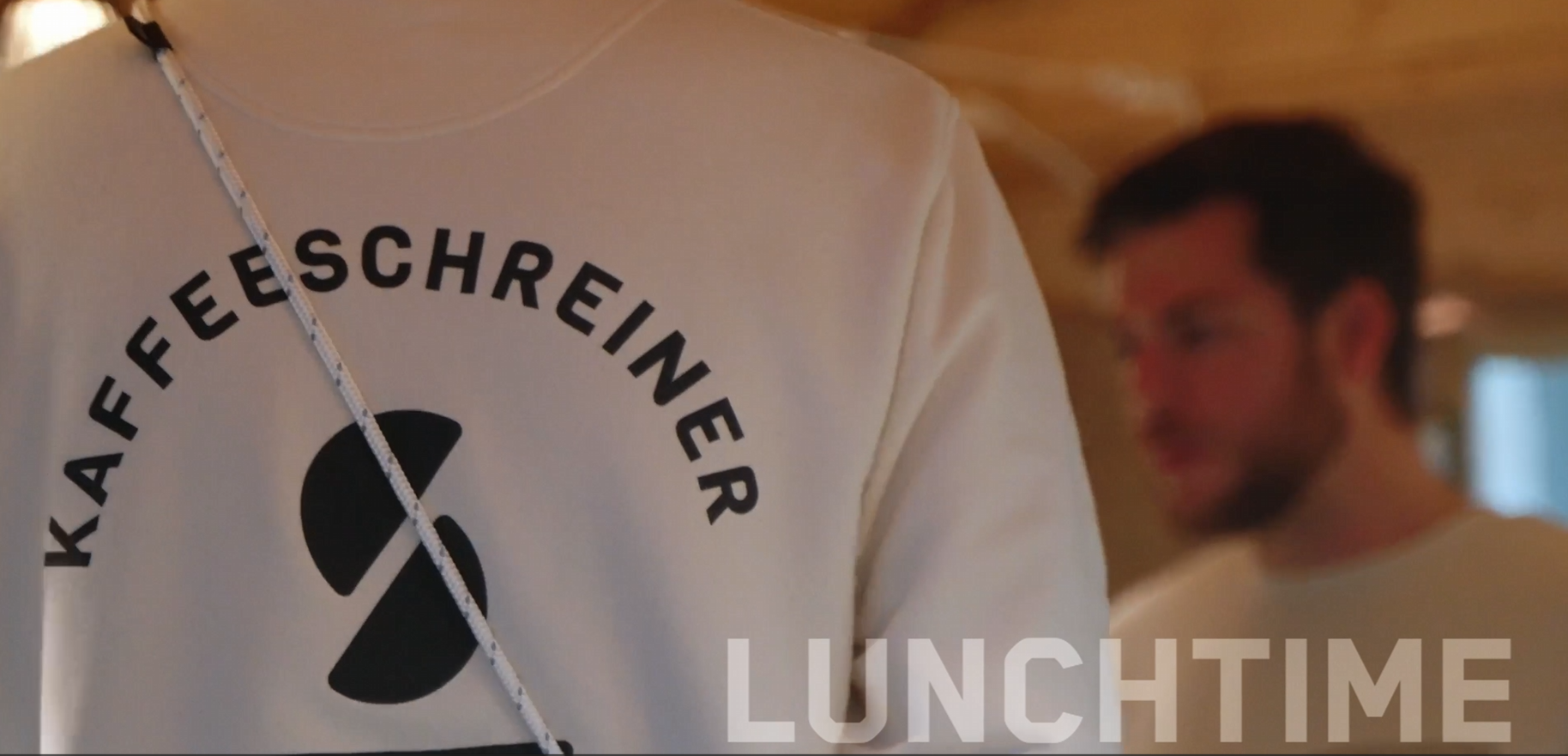 Ein angeschnittener Pulli von hinten deutet an, dass es sich um unseren Kooperationspartner "Kaffee Schreiner" handelt. Unten rechts stehen die Lettern "Lunchtime" angeschnitten.