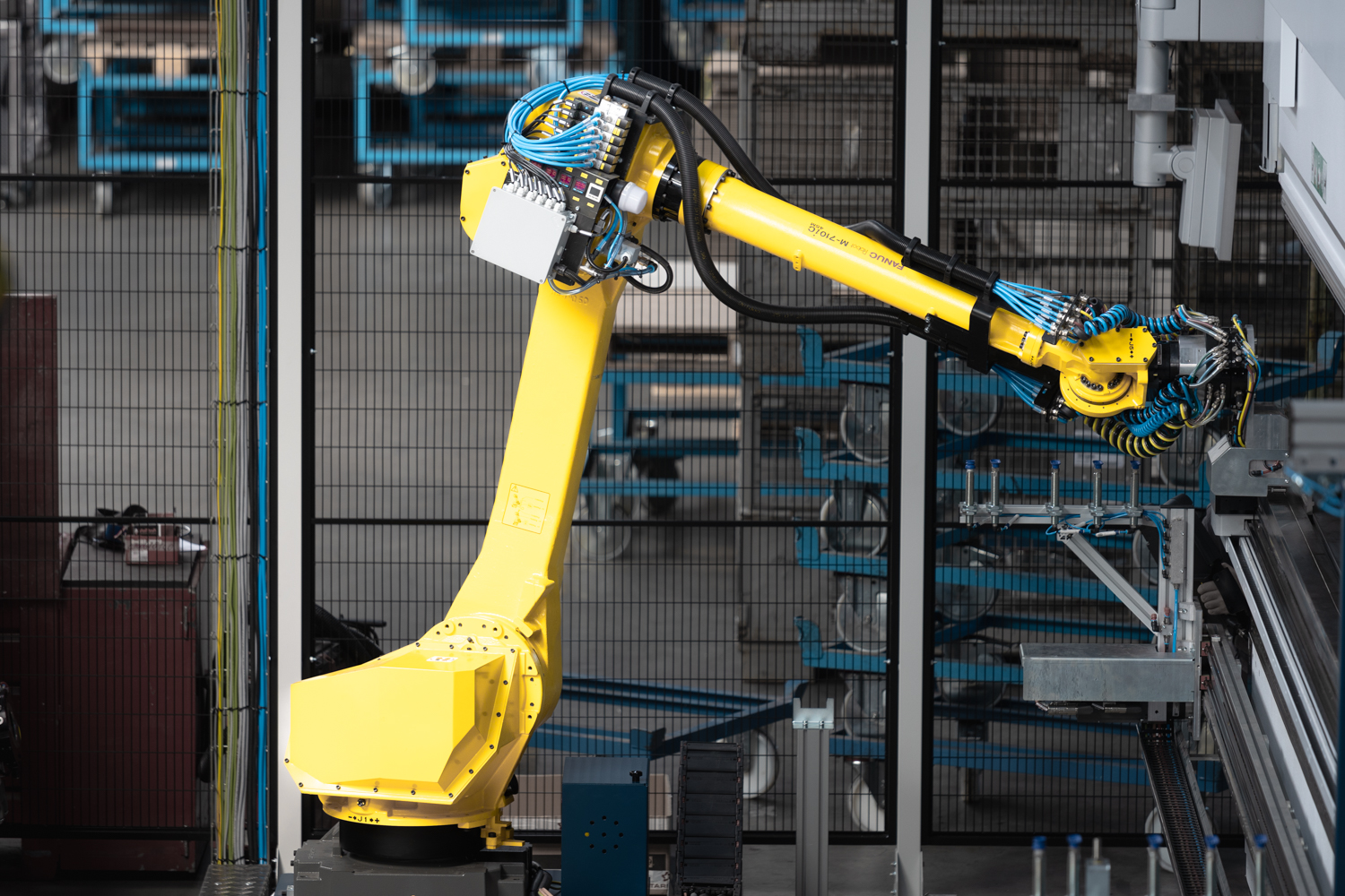 Ein gelber Roboterarm steht in einer Zelle.